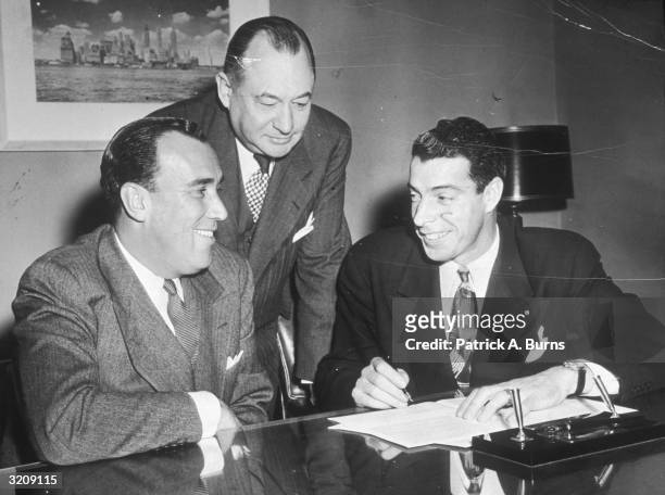 Joe DiMaggio signs a contract with the New York Yankees for the 1949 season in front of co-owner Dan Topping and general manager George Weiss .