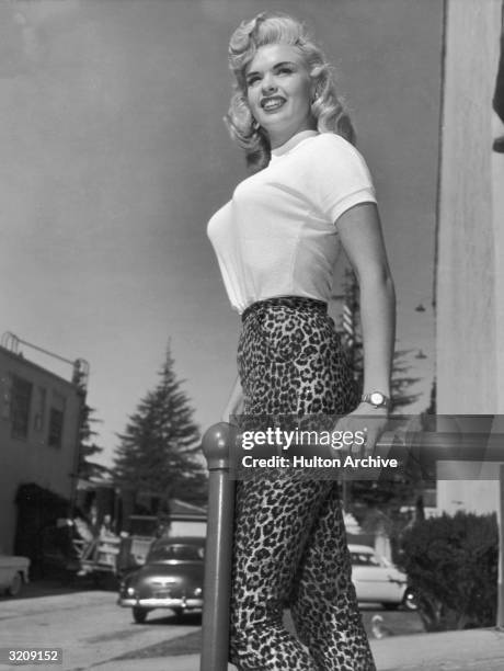 Portrait of American actor Jayne Mansfield standing outdoors in a light-colored T-shirt and leopard print pants.