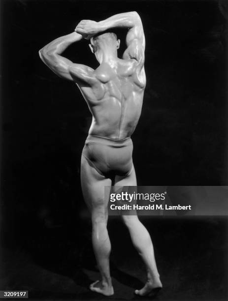 Full-length studio portrait of a male body builder flexing his back and shoulder muscles.