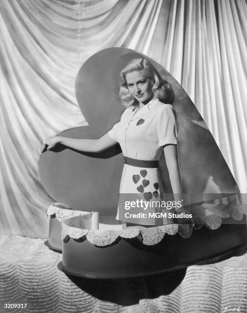 American actor Marilyn Maxwell, posing in a Valentine's outfit, pops out of a heart-shaped box in a promotional portrait for director Willis...