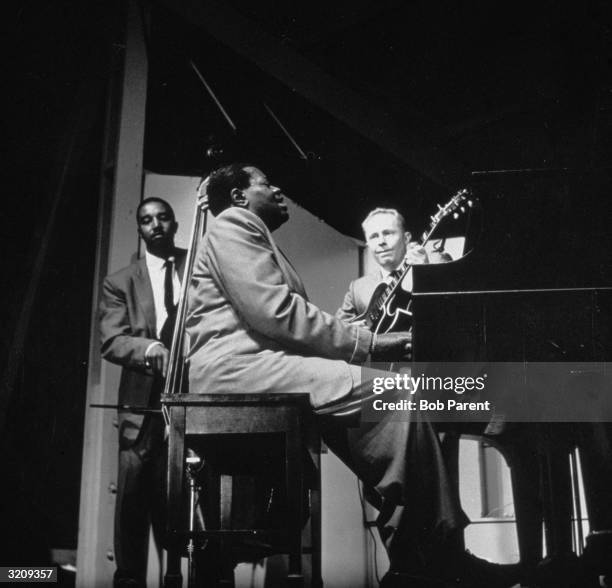 Canadian jazz pianist Oscar Peterson performing on stage with The Oscar Peterson Trio .