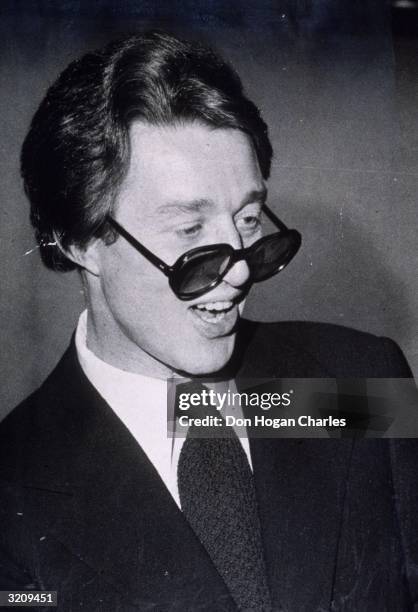 Candid portrait of American fashion designer Halston wearing dark sunglasses pushed down to the tip of his nose, New York City. He designed hats and...