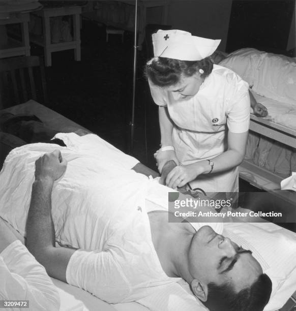 Nurse prepares the arm of a fireman who is donating blood to the Red Cross as part of the homefront War effort, World War II, New York City.