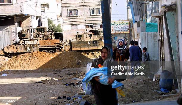 Palestinian family walks in front of Israeli tanks during an army operation to uncover tunnels at the Rafah refugee camp April 3, 2004 in the...