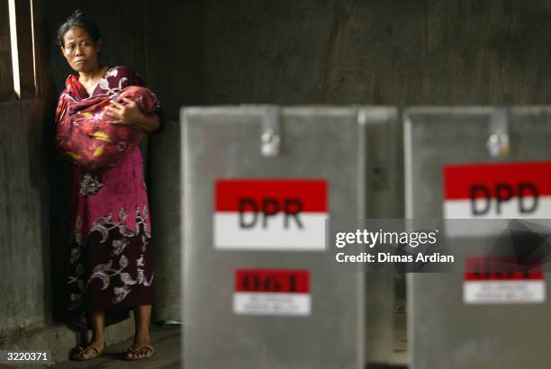 Woman holding a baby stands behind ballot boxes that are readied to be opened and counted April 5, 2004 in Jakarta, Indonesia. Around 147 million...