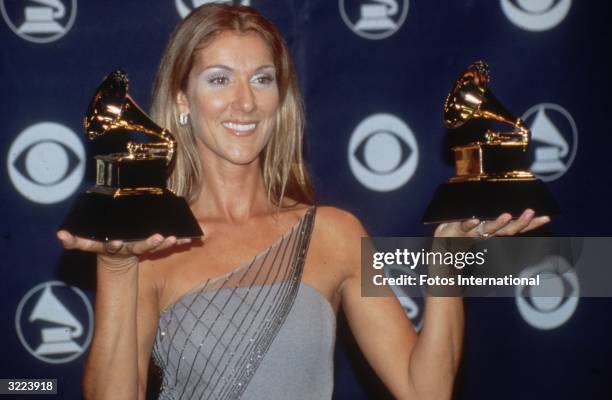 Canadian vocalist Celine Dion holding her two Grammys at the Grammy Awards, Los Angeles, California. Dion wears a beaded grey off-the-shoulder gown.
