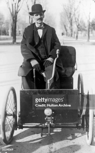 Portrait of American industrialist and inventor Henry Ford , wearing a derby hat and a three-piece suit, sitting outdoors in his first automobile, a...
