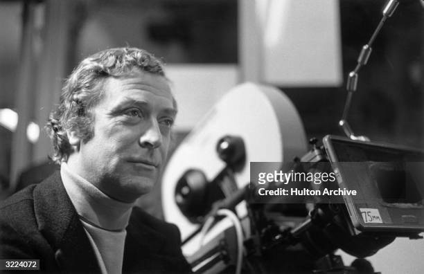 British actor Michael Caine stands next to a 75mm motion picture camera on the set of director Brian De Palma's film, 'Dressed to Kill'. Caine wears...