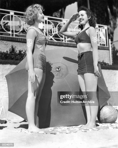 Full-length image of actors Elaine Morey and Peggy Moran wearing military sun tattoos on their arms.