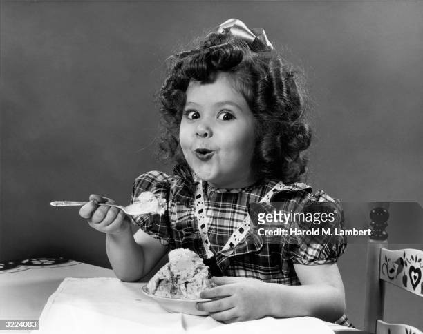 Portrait of a little girl in a plaid dress eating a bowl of ice cream and making a happy face.