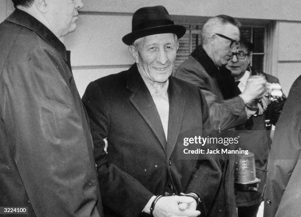 Mob boss Carlo Gambino smiles while standing in handcuffs after being arrested by the FBI.