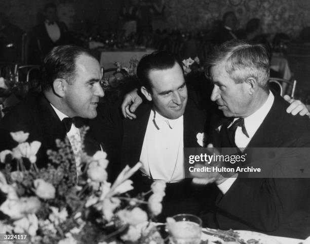 American film producer Hal Roach, comic actor Harold Lloyd, and humorist Will Rogers sit and talk at a table during an event in honor of Roach.