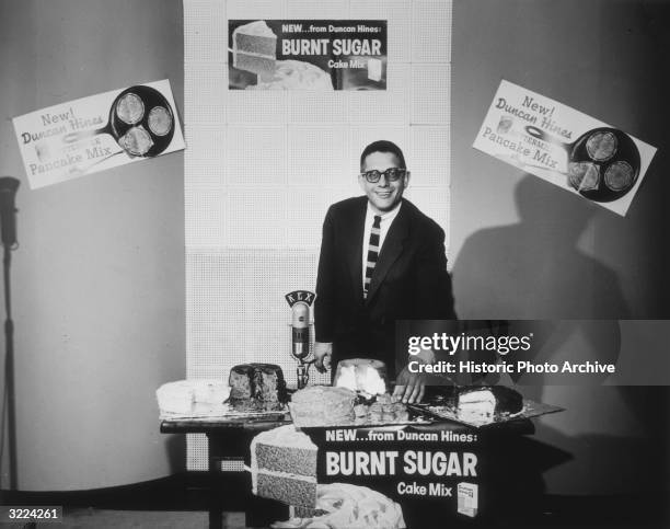 Portrait of a KEX radio host standing behind a table displaying cakes made from Duncan-Hines Burnt Sugar Cake Mixes, Portland, Oregon. The station...