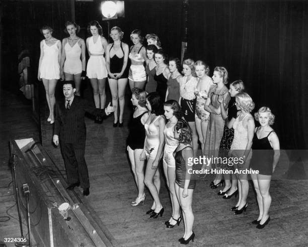 American theater producer Billy Rose stands at the front of a stage, gesturing in front of two lines of young showgirls who were performing in one of...