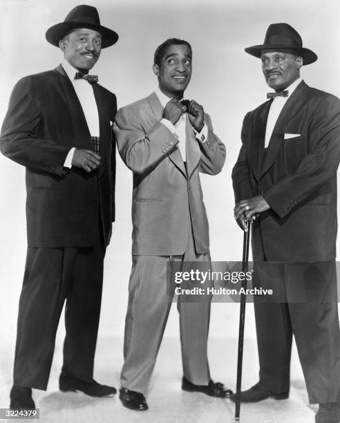 Full-length studio portrait of American singer, dancer and actor Sammy Davis Jr. Adjusting his tie between his father, Sammy Davis Sr. , and Will...