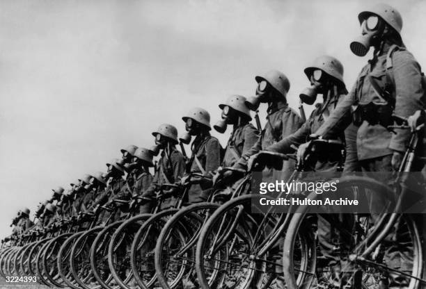 Full-length view of members of the German light machine-gun Cyclist Corps wearing gas masks while standing next to their bicycles in a lineup in...