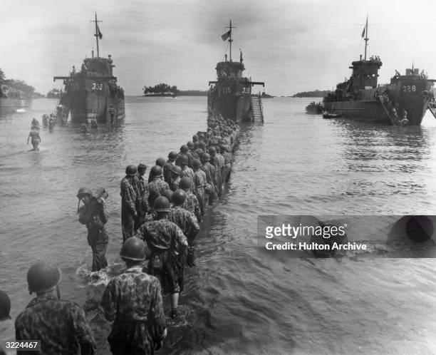 United States Marines, in camouflage, form a line in the surf to pass munitions from three landing craft carriers onto the shore during the seizure...