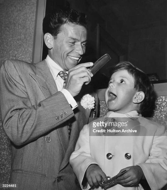 American singer and actor Frank Sinatra combs the hair of his son, Frank Jr, on the set of director Richard Whorf's film, 'It Happened in Brooklyn,'...