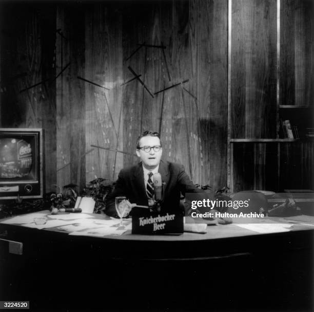 American comedian and talk show host Steve Allen sitting at a desk speaking during an episode of 'The Tonight Show'. An advertisement for...