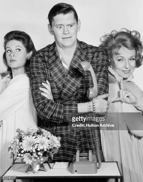 American actors Elizabeth Montgomery, Dick York, and Agnes Moorehead, all wearing sleepwear, looking at a telephone with a levitating receiver, in a...