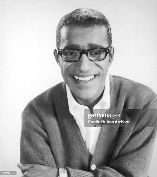 Headshot studio portrait of American singer, actor, and dancer Sammy Davis Jr. Wearing eyeglasses and a cardigan sweater.