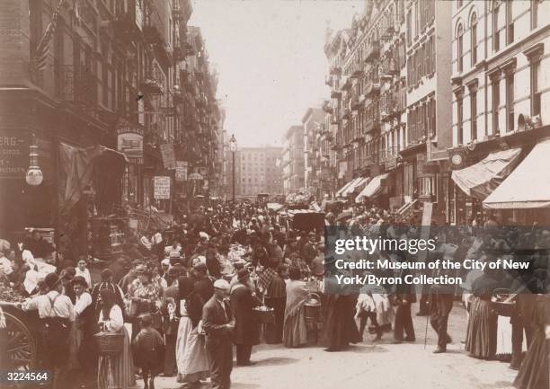 Crowded outdoor market on Orchard Street, looking south from Hester Street, on the Lower East Side, New York City. Some of the signs hanging from...