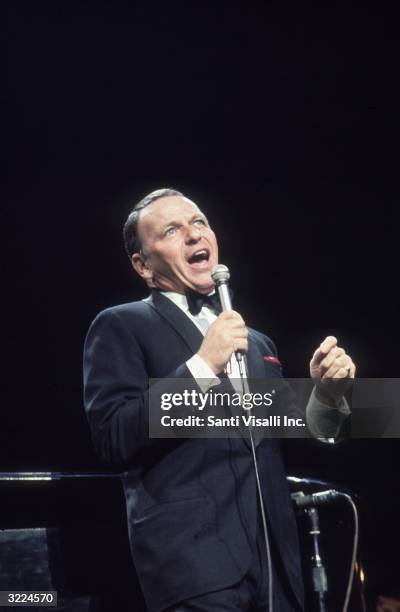 American singer and actor Frank Sinatra , wearing a tuxedo with a red handkerchief in the pocket, singing with his mouth wide open at anti-defamation...