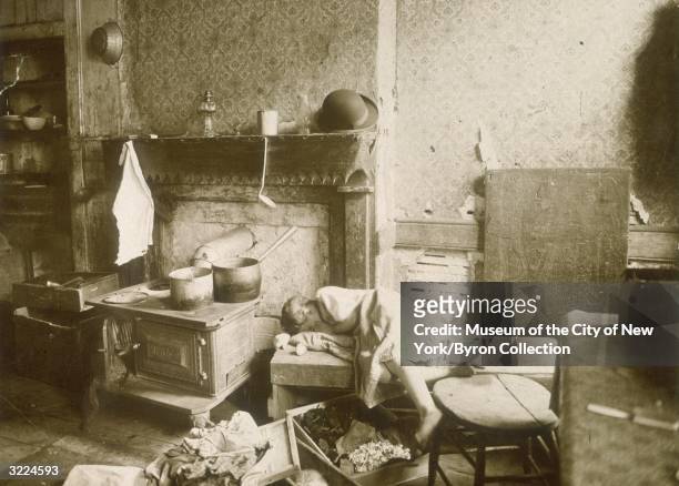 Child slumped over a bench next to a bricked up fireplace and a stove, in a dilapidated tenement apartment on the Lower East Side of New York City.