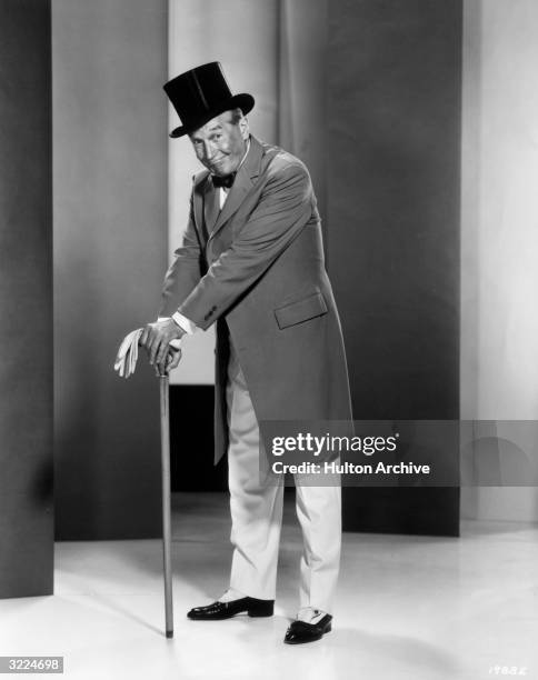 Full-length promotional portrait of French actor and singer Maurice Chevalier , wearing a top hat and standing with his hands folded atop his cane,...