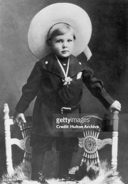 Full-length portrait of American actor Gary Cooper as a young boy, standing atop two chairs and wearing a wide-brimmed hat.