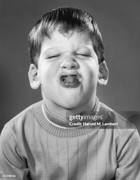 Studio headshot of a boy sticking his tongue out and squinting his eyes shut.