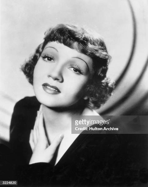 Headshot studio portrait of French-born actor Claudette Colbert wearing a lowcut velvet top and her trademark short fringe hairstyle.