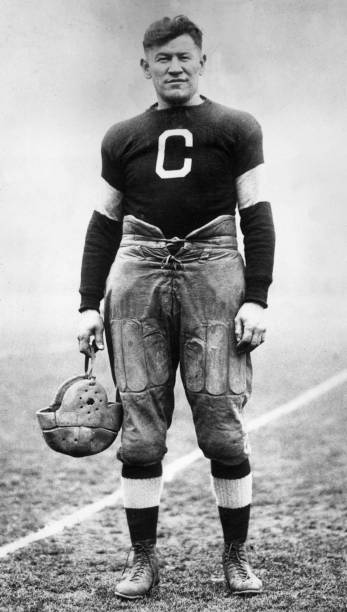 Full-length portrait of American athlete Jim Thorpe posing in a football uniform on a field.