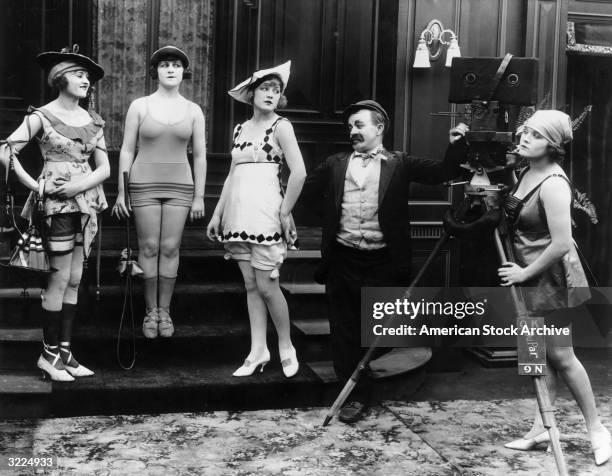 American actor Chester Conklin looks on while Mack Sennett's Bathing Beauties pose on a staircase during the filming of one of the director's silent...