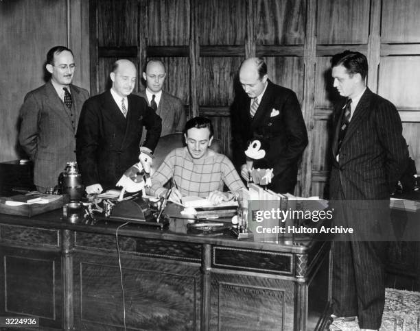 American animator and producer Walt Disney is surrounded by a group of executives while seated at his desk in his office. Donald Duck and Mickey...