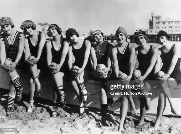 Mack Sennett Bathing Beauties cross their legs while posing on a wooden boat on a beach in a film still.