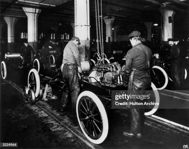 Workers constructing a Model-T engine on an assembly line in a Ford Motor Company factory.