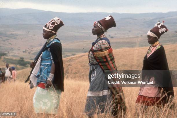 Swazi women, wearing shawls and headdresses, walking outdoors in a field on their way to a wedding.