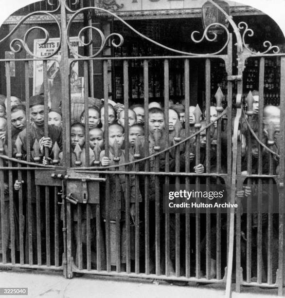 Cantonese boys and men crowd behind the Gate of the English Bridge, which barred the Cantonese from the English legations during the Boxer Rebellion,...