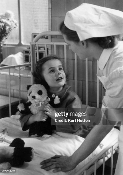 Nurse talking to a young patient and her toy panda while making her rounds at a London Children's Hospital.