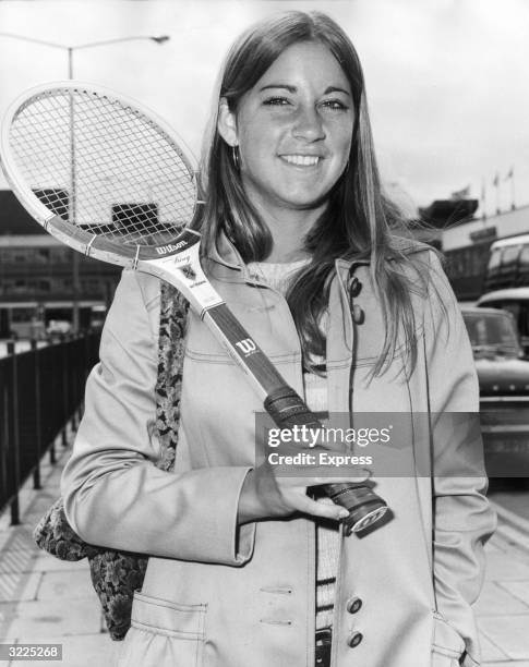 Portrait of American tennis player Chris Evert, wearing a coat and holding a tennis racket over her shoulder, in London to compete in her first...