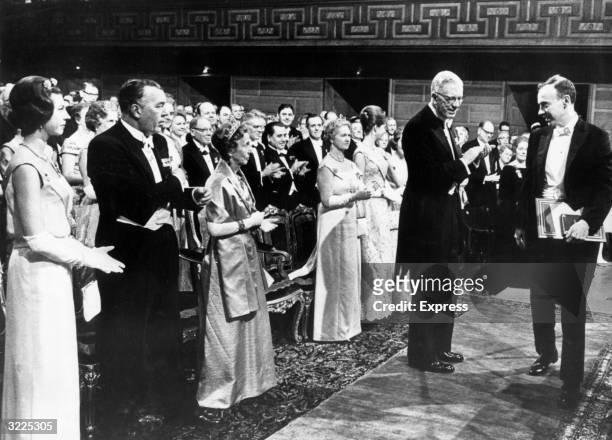 American biochemist James Dewey Watson receiving the Nobel Prize for Chemistry, before a standing, applauding crowd dressed in formal attire,...