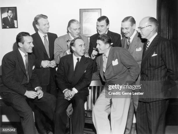 American actor and politician Ronald Reagan leans against a chair and holds a cigar while talking with seven members of the Screen Actors Guild,...
