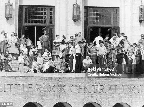 View of National Guardsmen standing outside Little Rock Central High School and a large group of white students standing with them to prevent any...