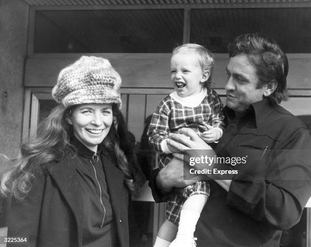 Married American country singers Johnny Cash and June Carter Cash pose with their eighteen month-old son John, Glasgow, Scotland. June wears a knit...