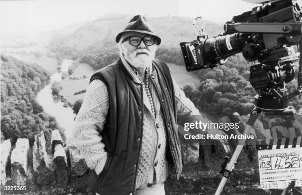British actor and film director Sir Richard Attenborough poses behind a motion picture camera and a clapperboard outdoors on the location set of his...
