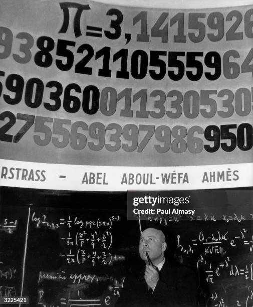 Man stands in front of a blackboard illustrating the pi number.