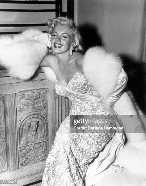 American actor Marilyn Monroe smiling as she sits at the home of director Jean Negulesco, after the premiere of his film, 'How to Marry a...