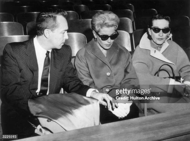 American actor Lana Turner , wearing dark sunglasses, sits next to her ex-husband, Stephen Crane, in a courtroom during the murder trial of their...
