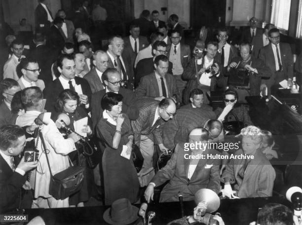 High-angle view of American actor Lana Turner seated in a courtroom, surrounded by reporters at the trial of her daughter, Cheryl Crane, for the...